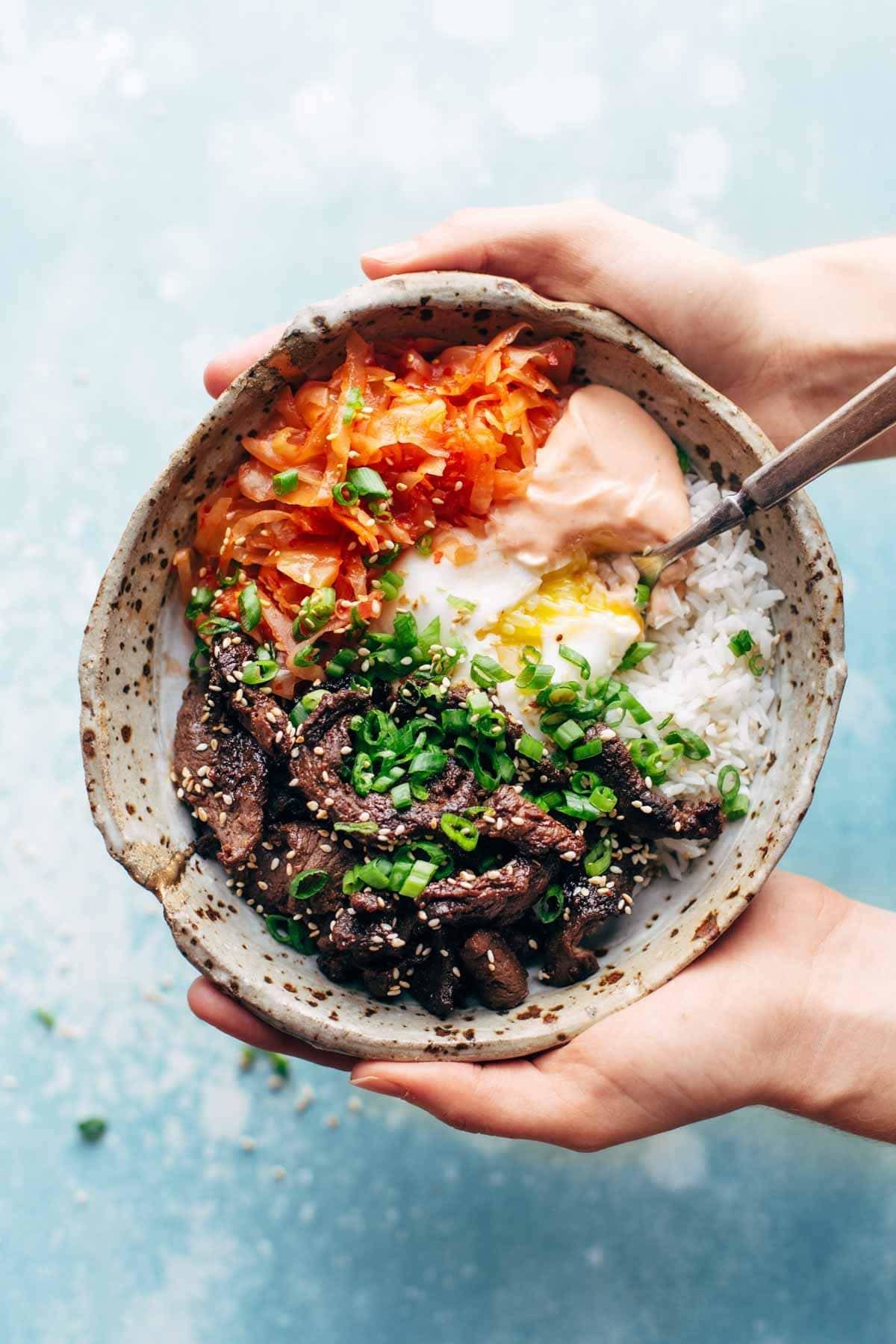 Hands holding a bowl with rice and steak.