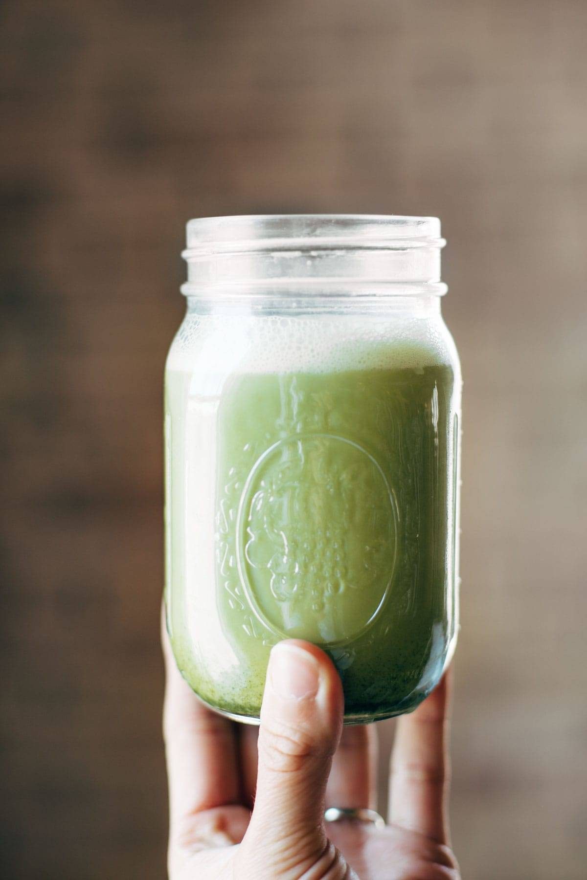 Iced Matcha Green Tea Latte shaken in a jar with a white hand holding it up.
