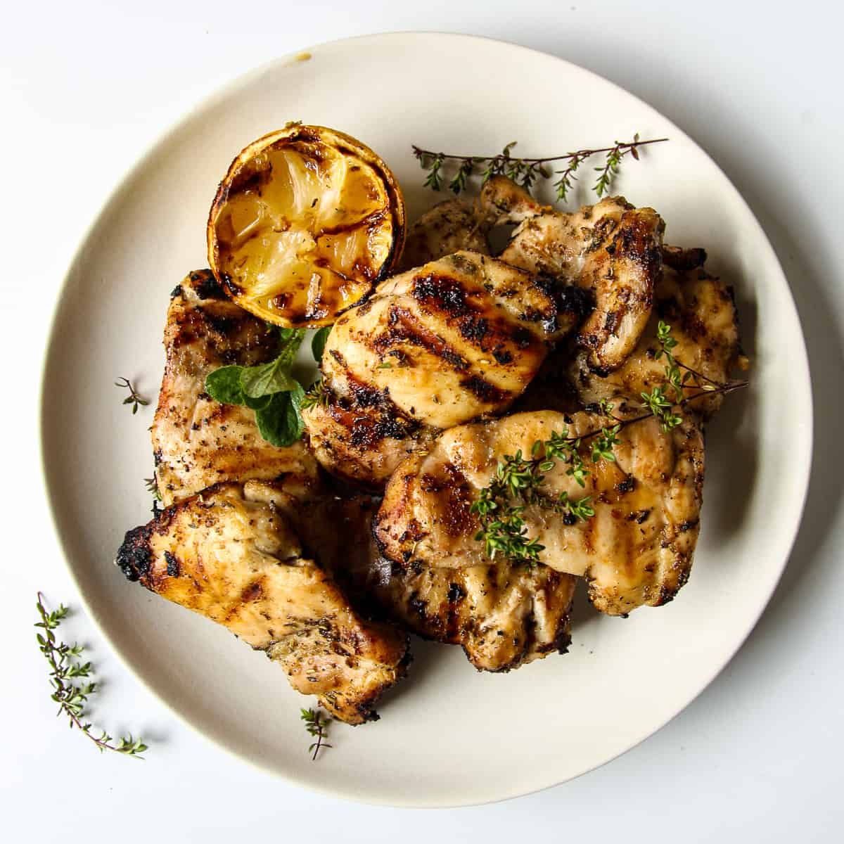 Grilled Boneless Chicken Thighs piled on a white plate garnished with thyme.