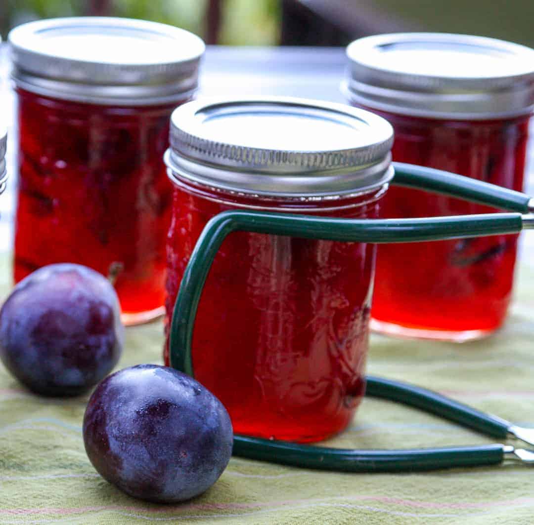 Three jars of jam and two plums on a table