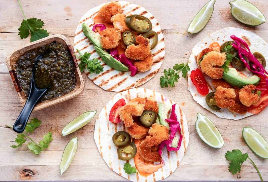 3 Coconut Shrimp Tacos with jalapeno slices, avocado slices and lime wedges