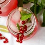 A drink garnished with red berries and a mint leaf
