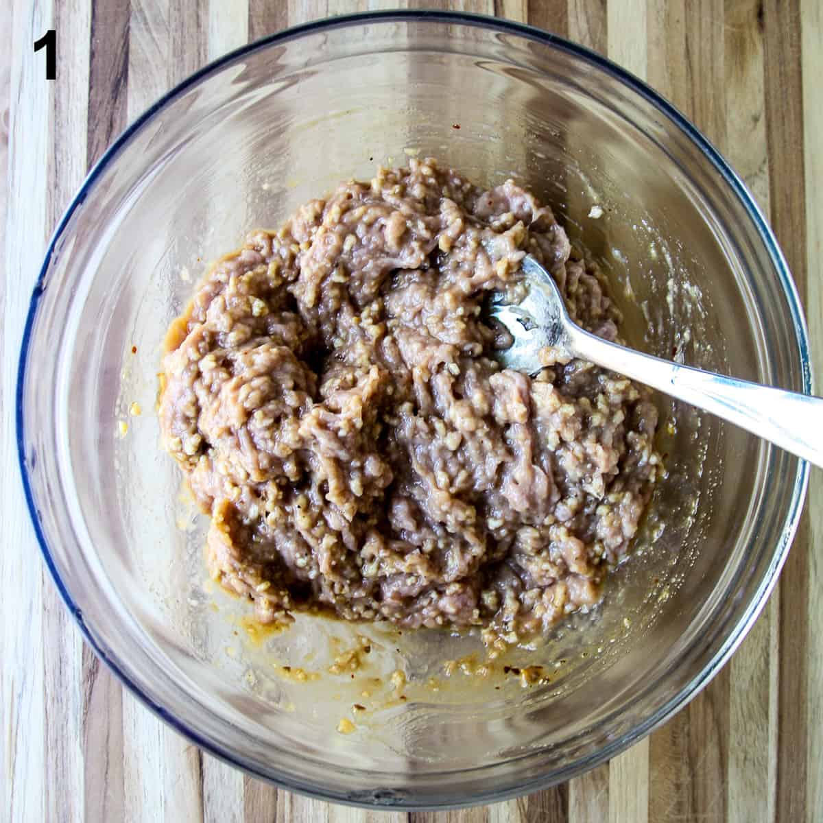 Step 1 of this recipe with meatball ingredients being combined in a glass mixing bowl.