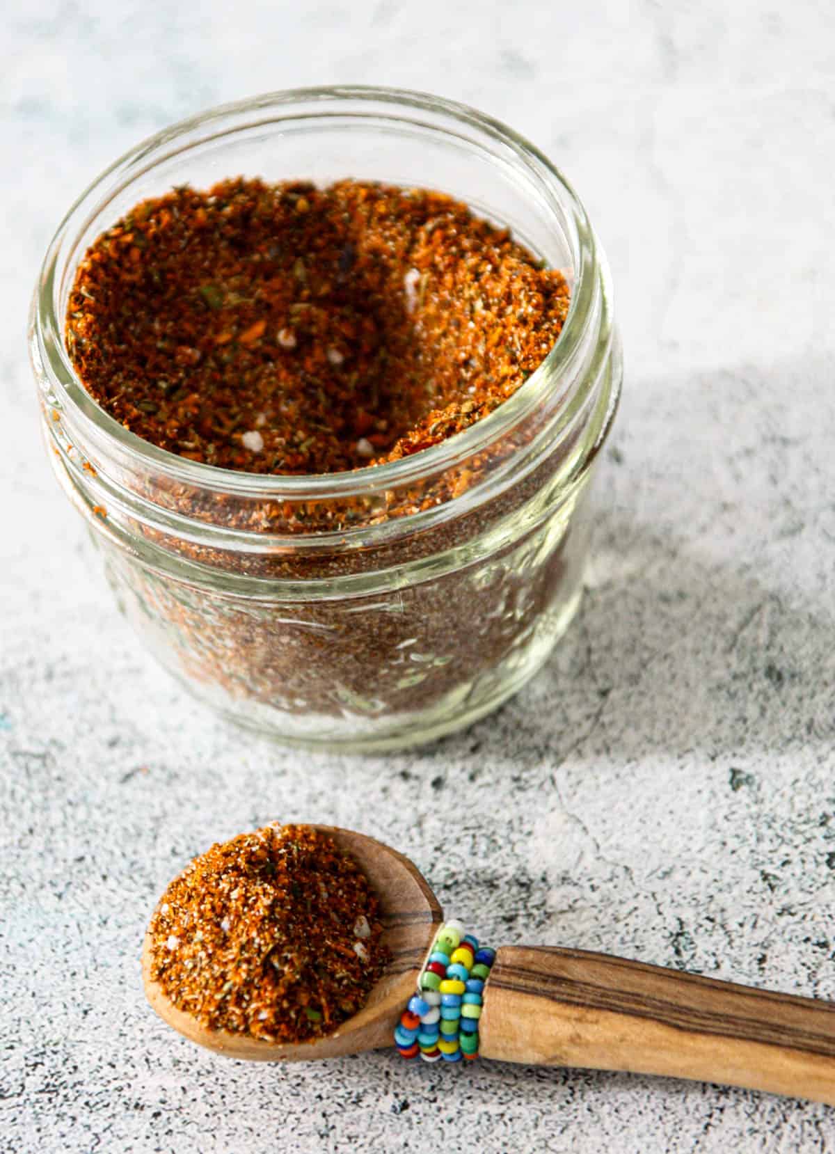 A jar of homemade Cajun seasoning next to a small wooden spoon.