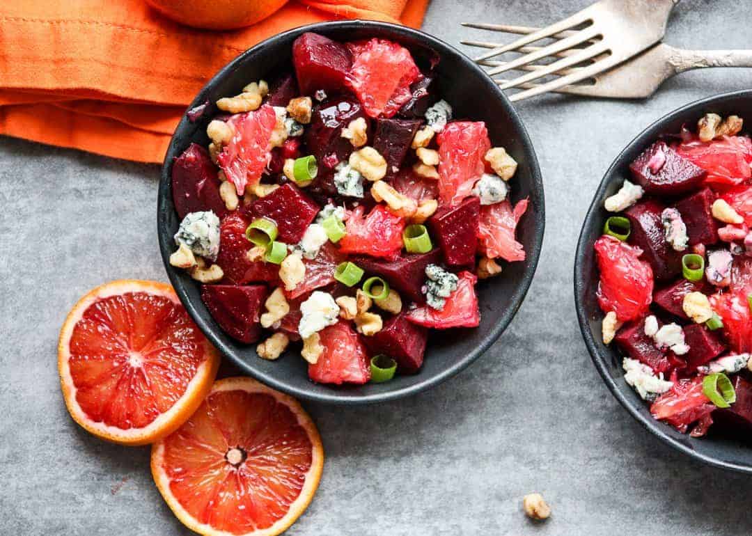Beet salad with grapefruit slices and blue cheese crumbles in black bowls