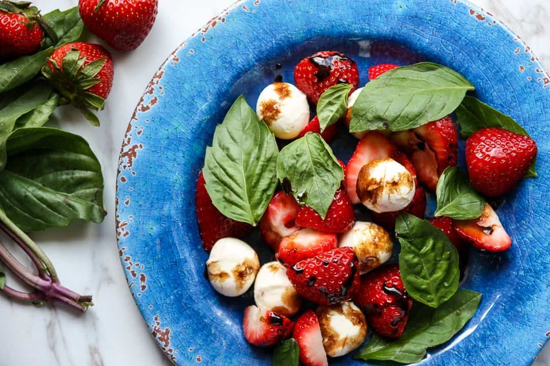 Top shot of basil, strawberries and mozzarella cheese balls on blue plate.