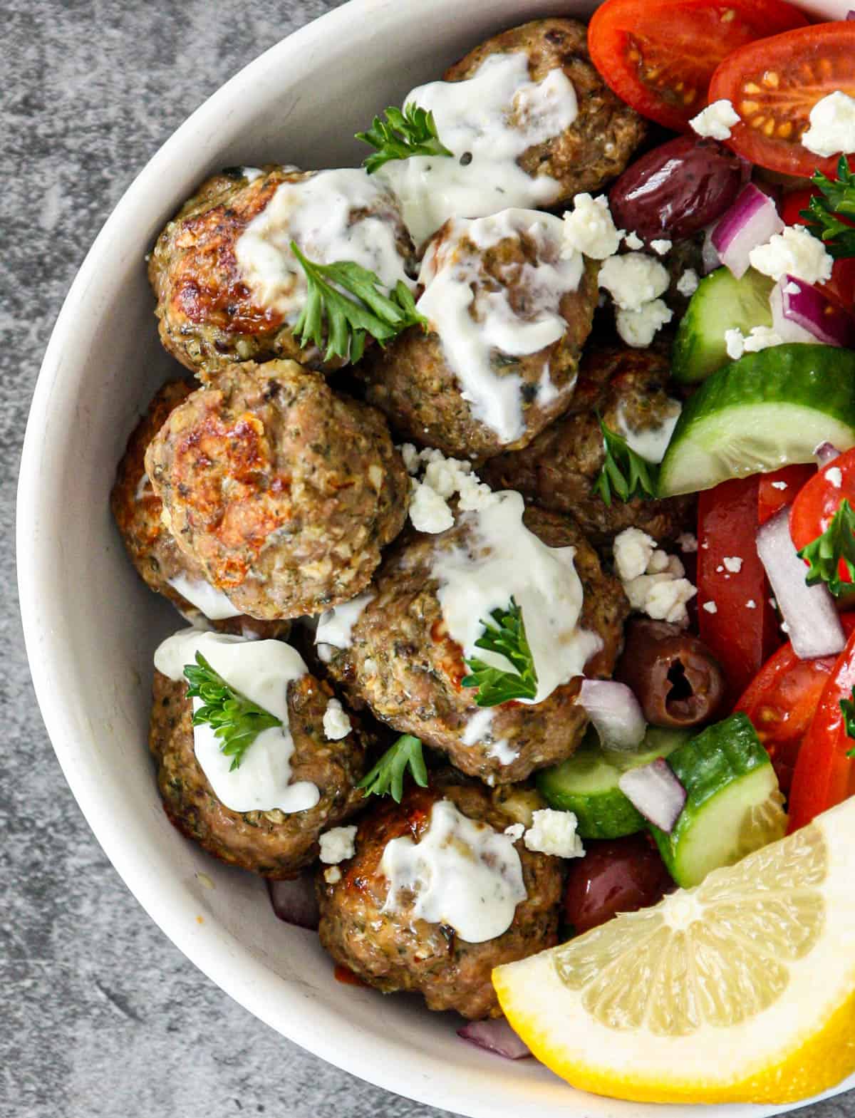 Greek chicken meatballs in a white bowl with salad and lemon wedges.