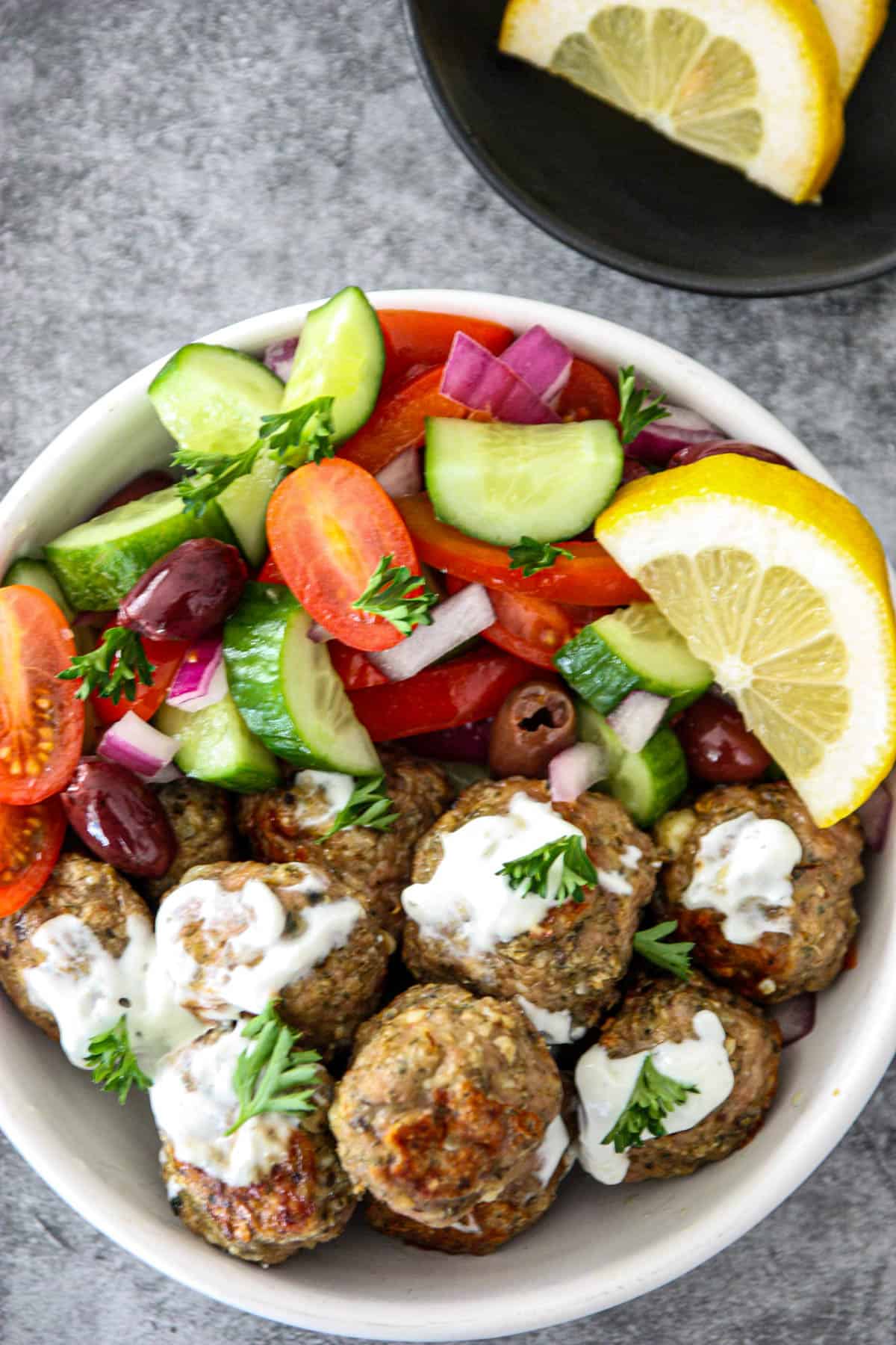 Greek chicken meatballs drizzled with tzatziki sauce in a white bowl. 