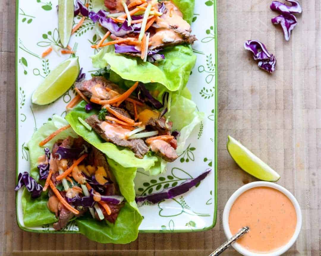 A plate of wraps with vegetables and steak, with a dish of sauce