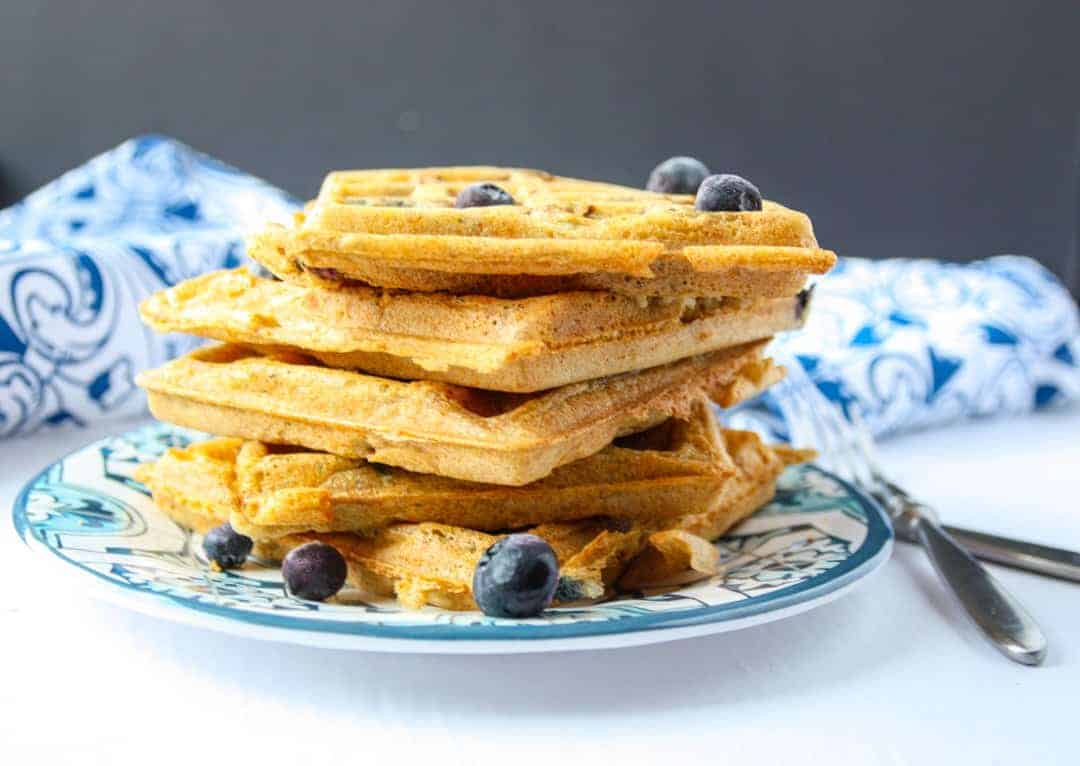 Five blueberry waffles stacked on a blue & white plate