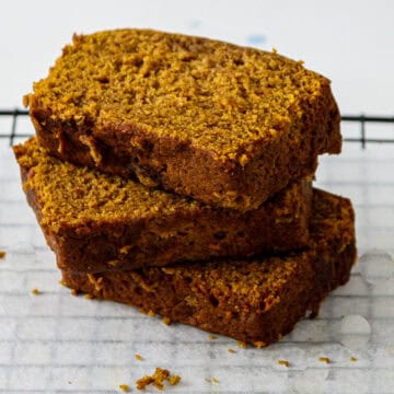 Three slices of gluten free pumpkin loaf stacked on a plate.