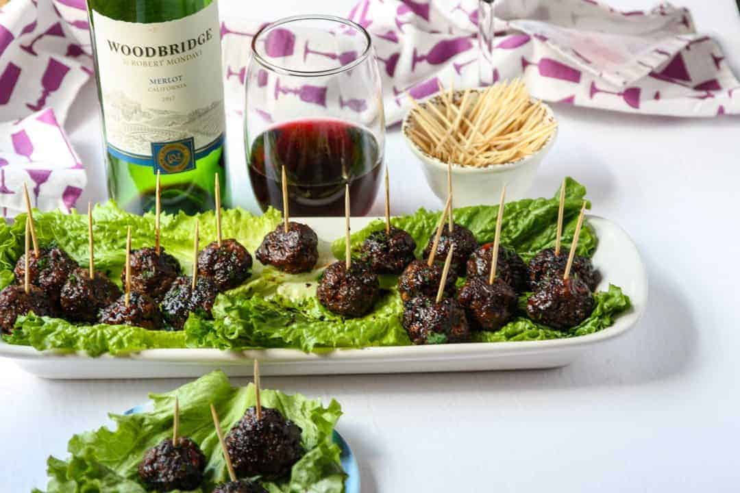 Tray of meatball appetizers on a bed of lettuce with a glass of red wine