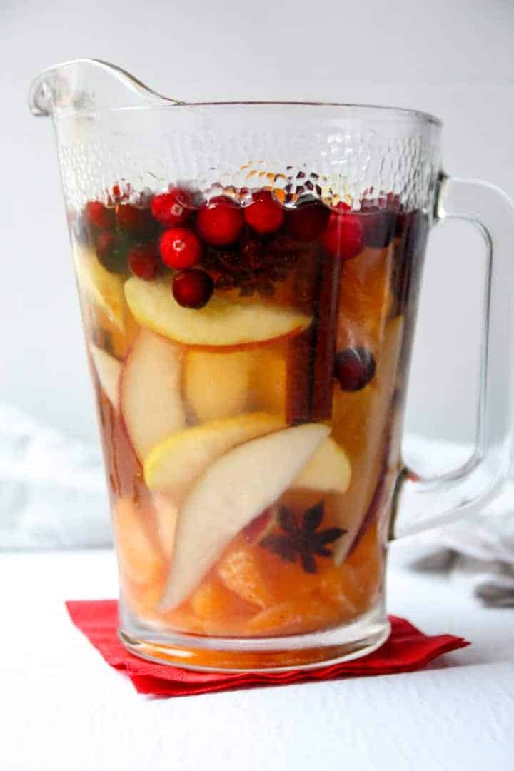 A carafe of sangria filled with cinnamon sticks, apple slices, orange slices, and cranberries