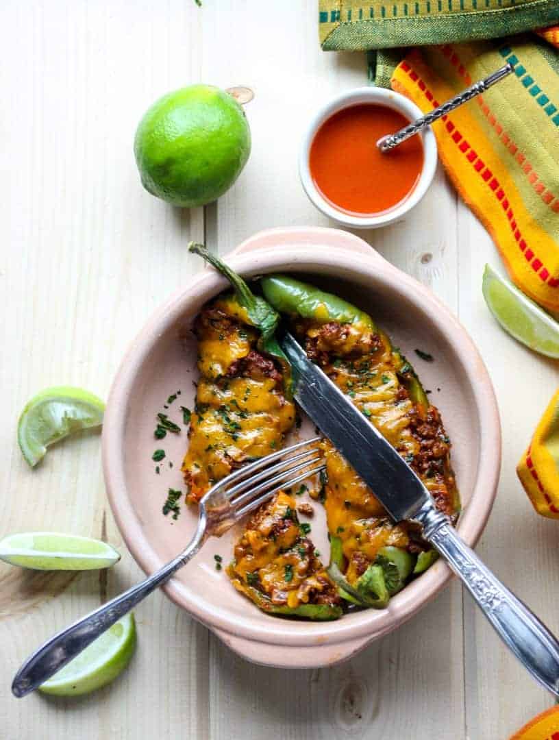 A bowl of food sitting on a table, with a lime and hot sauce