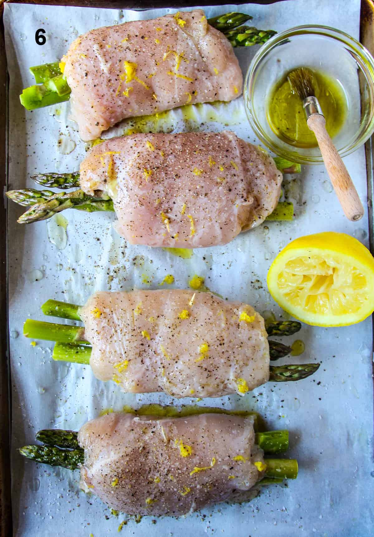 Uncooked asparagus stuffed chicken being brushed with olive oil.