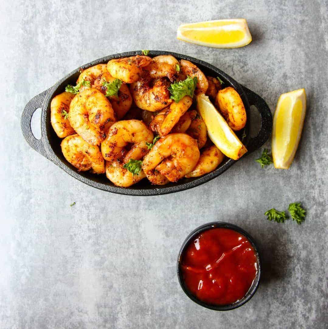 Shrimp in a pan on a table with lemon and sauce