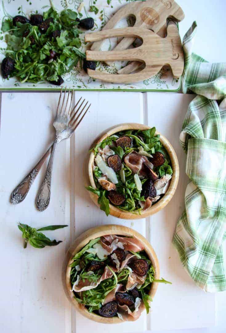Two wooden bowls of fig salad beside a half empty salad platter