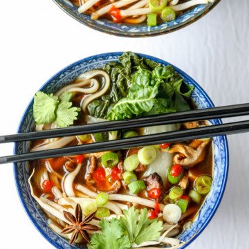 A bowl of vegetables and noodles with chopsticks