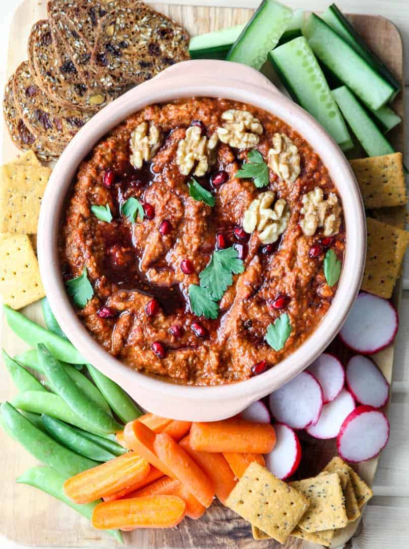 A bowl of dip on a table with vegetables and crackers