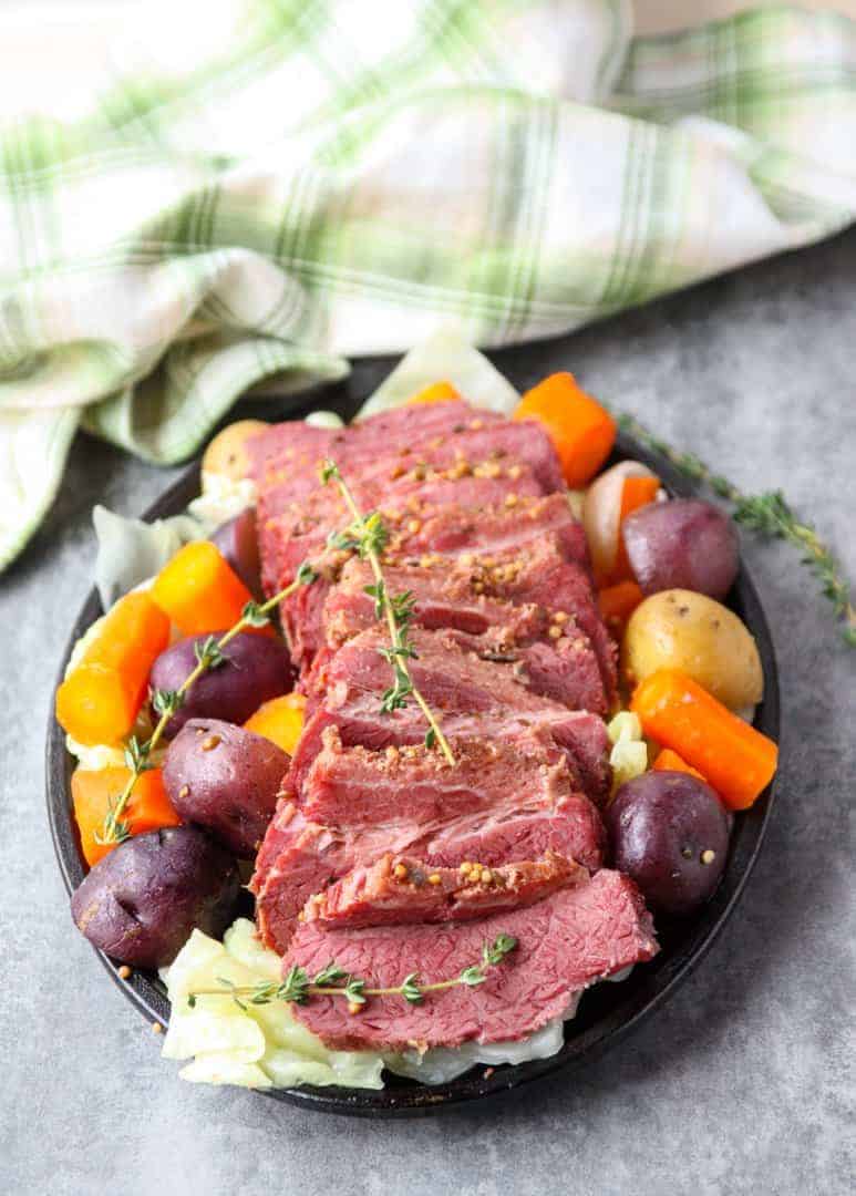 A round black plate of vegetables and slow cooker corned beef and cabbage