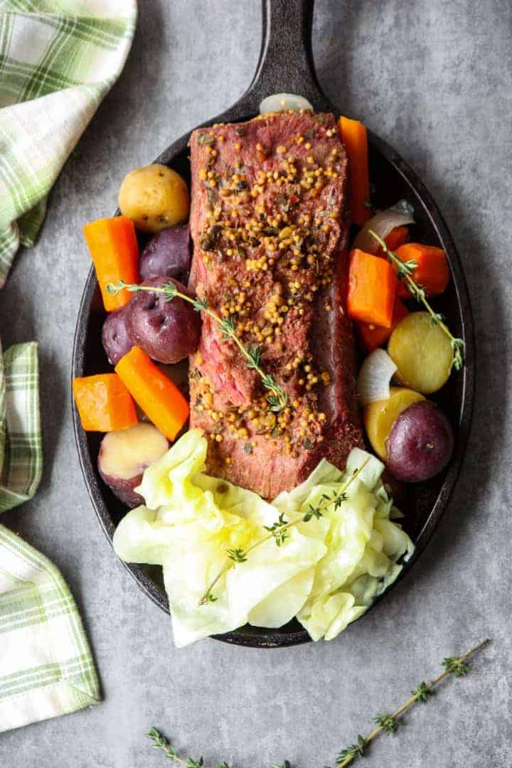 A round black plate of vegetables and slow cooker corned beef and cabbage.