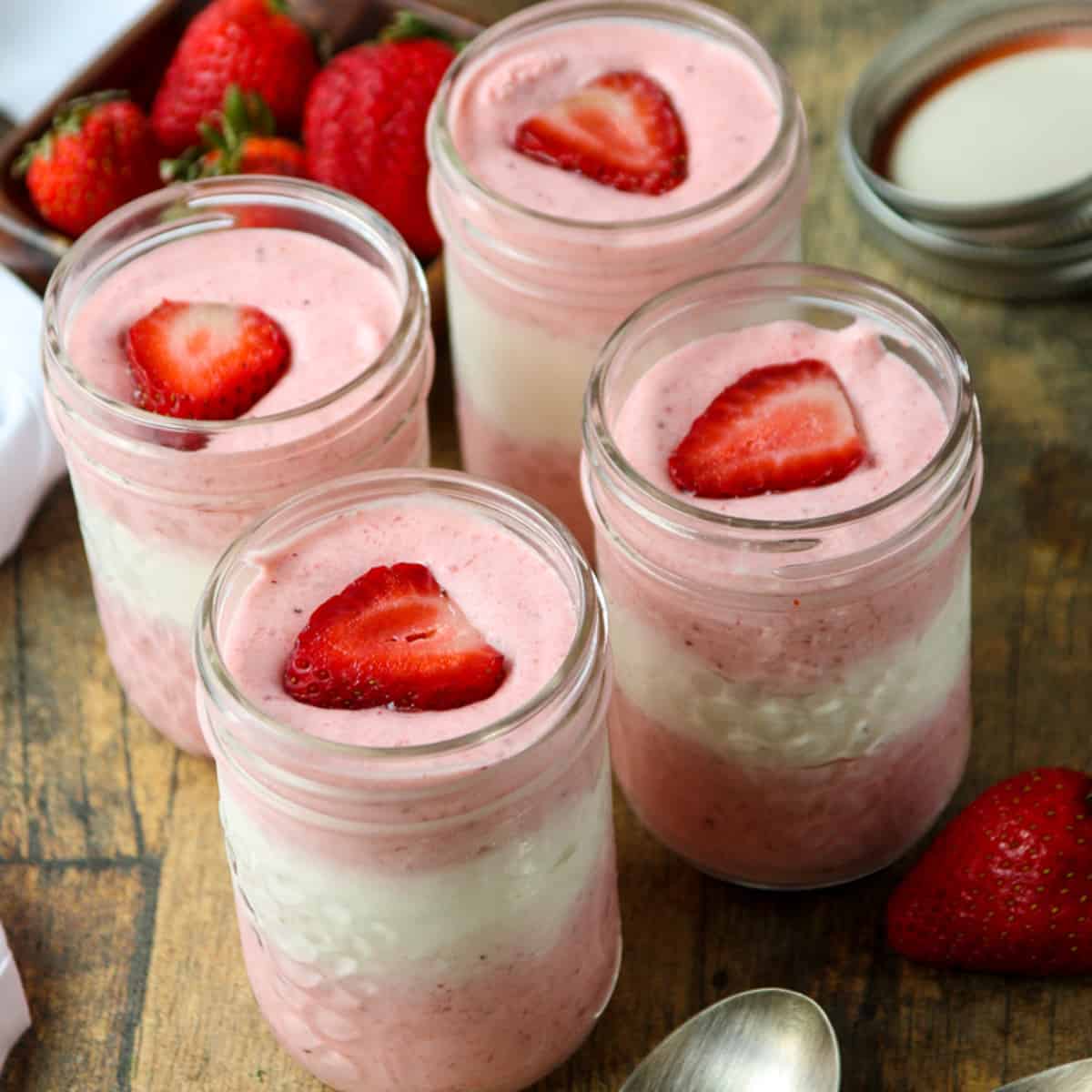 Four jars of mousse on a wooden table.