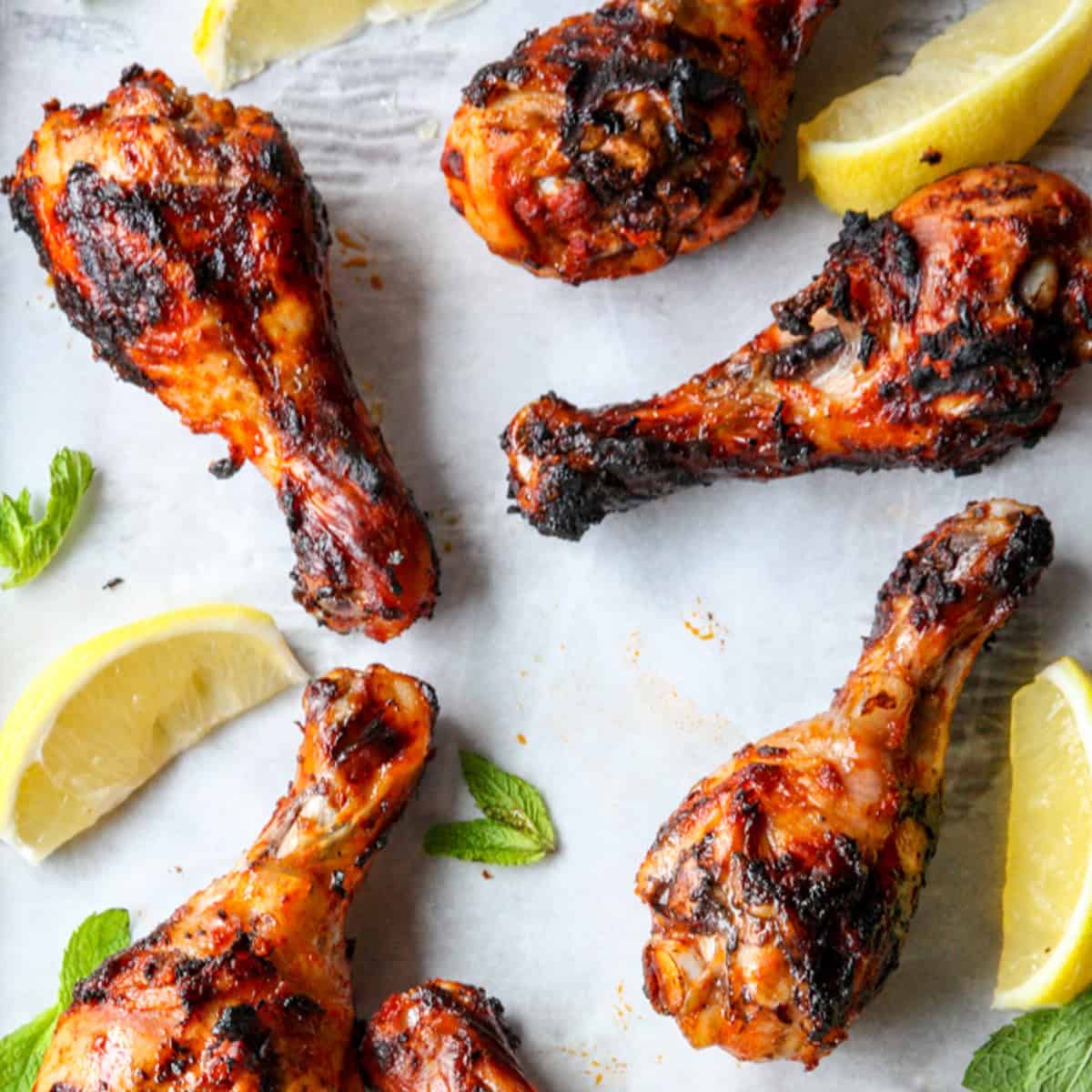 Four grilled harissa chicken drumstick with lemon wedges on a platter.