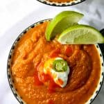 A close up of a bowl of soup with lime wedges
