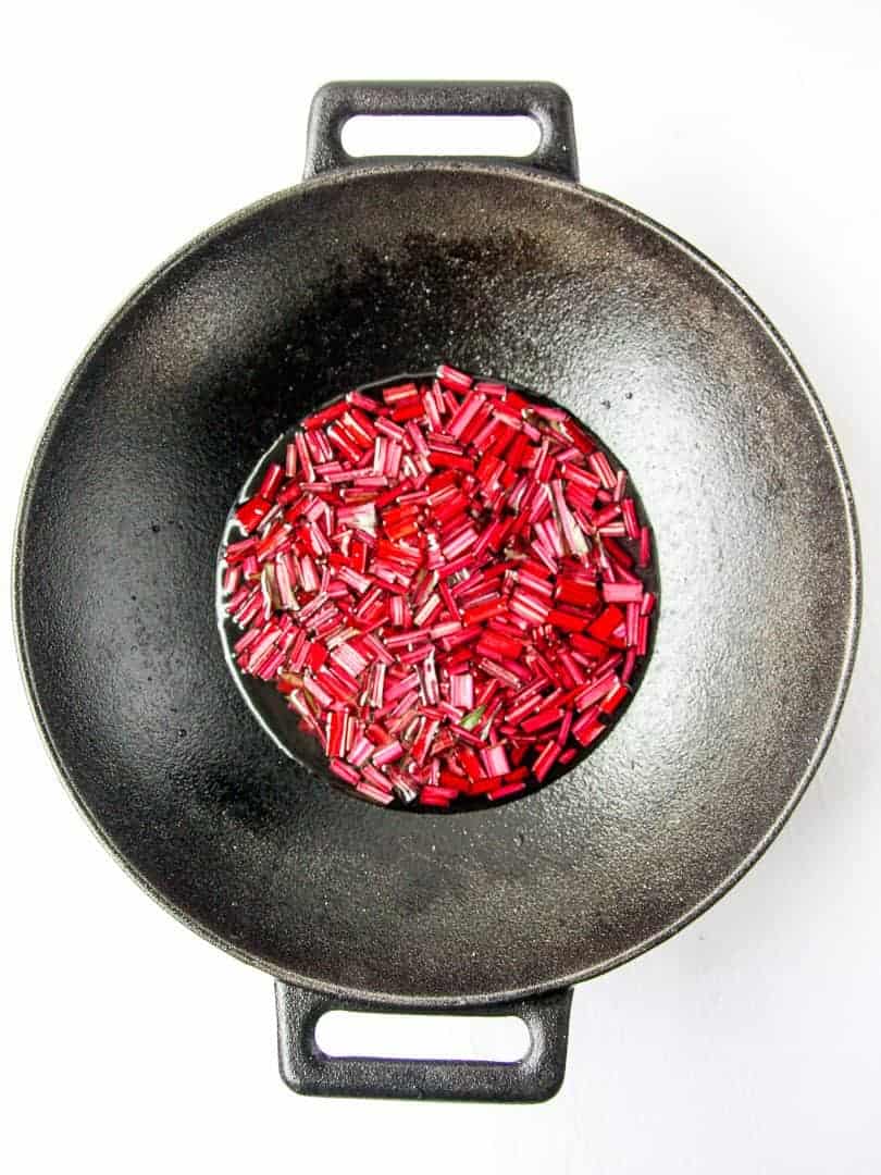 Red, chopped beet green stems cooking in a pan with water.