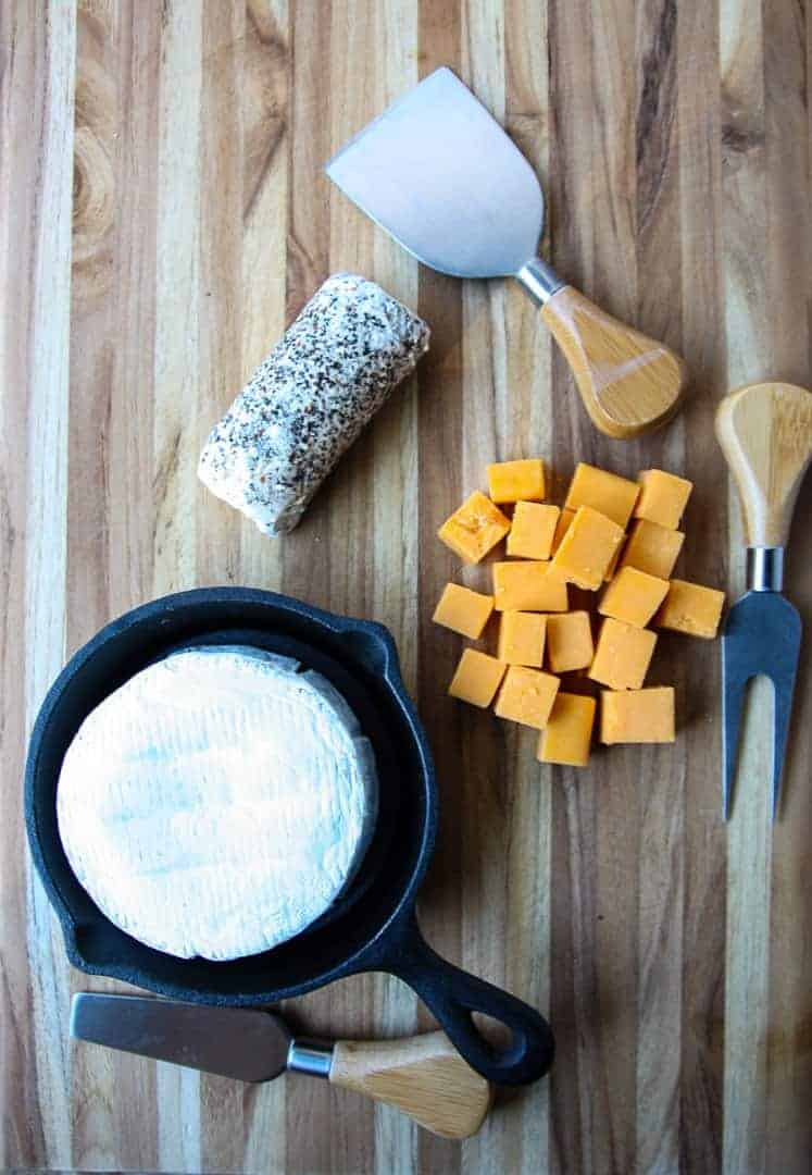 A wooden cutting board with various types of cheese on it