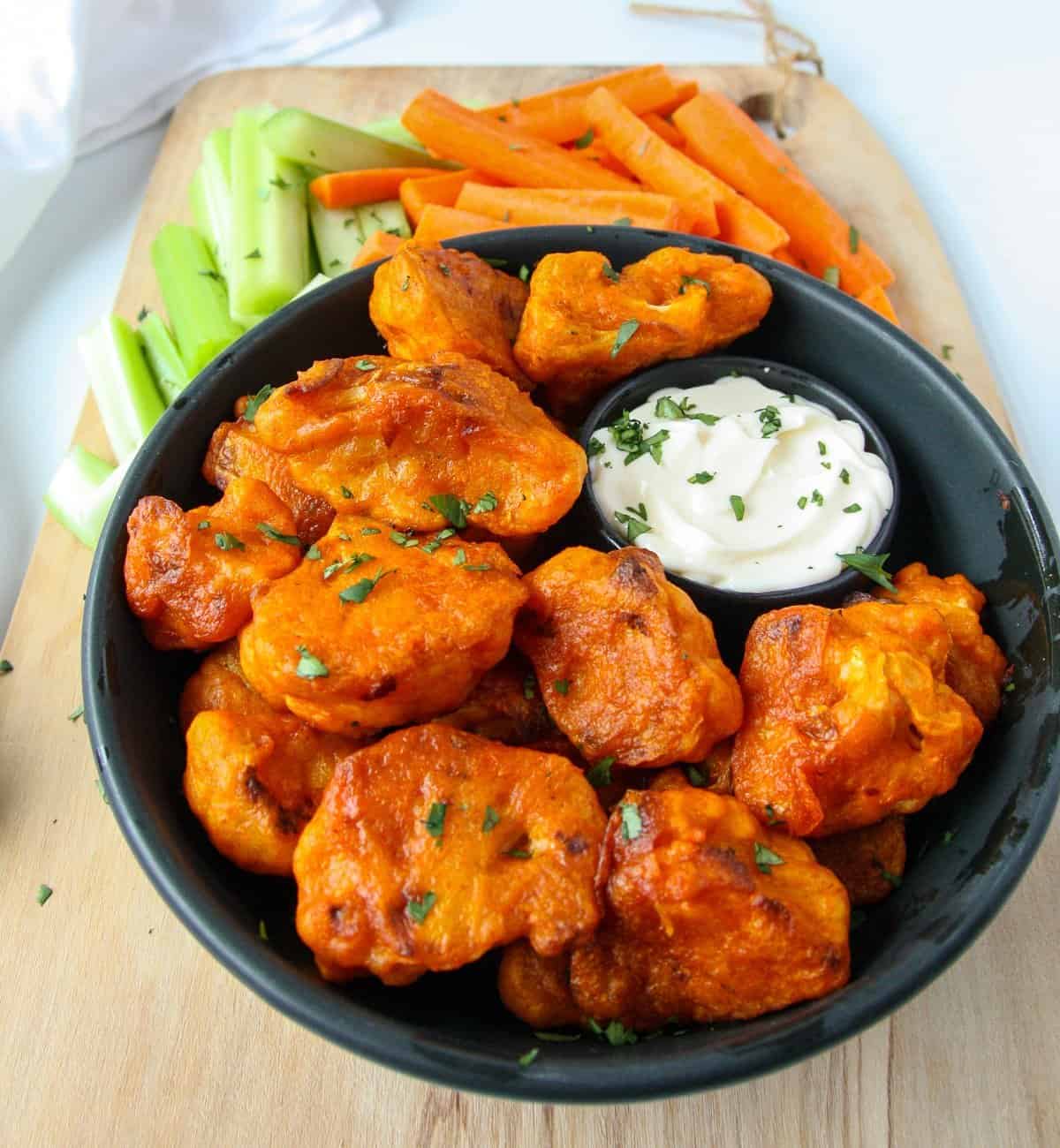 Gluten-free baked buffalo cauliflower bites on a black plate with carrot and celery sticks.