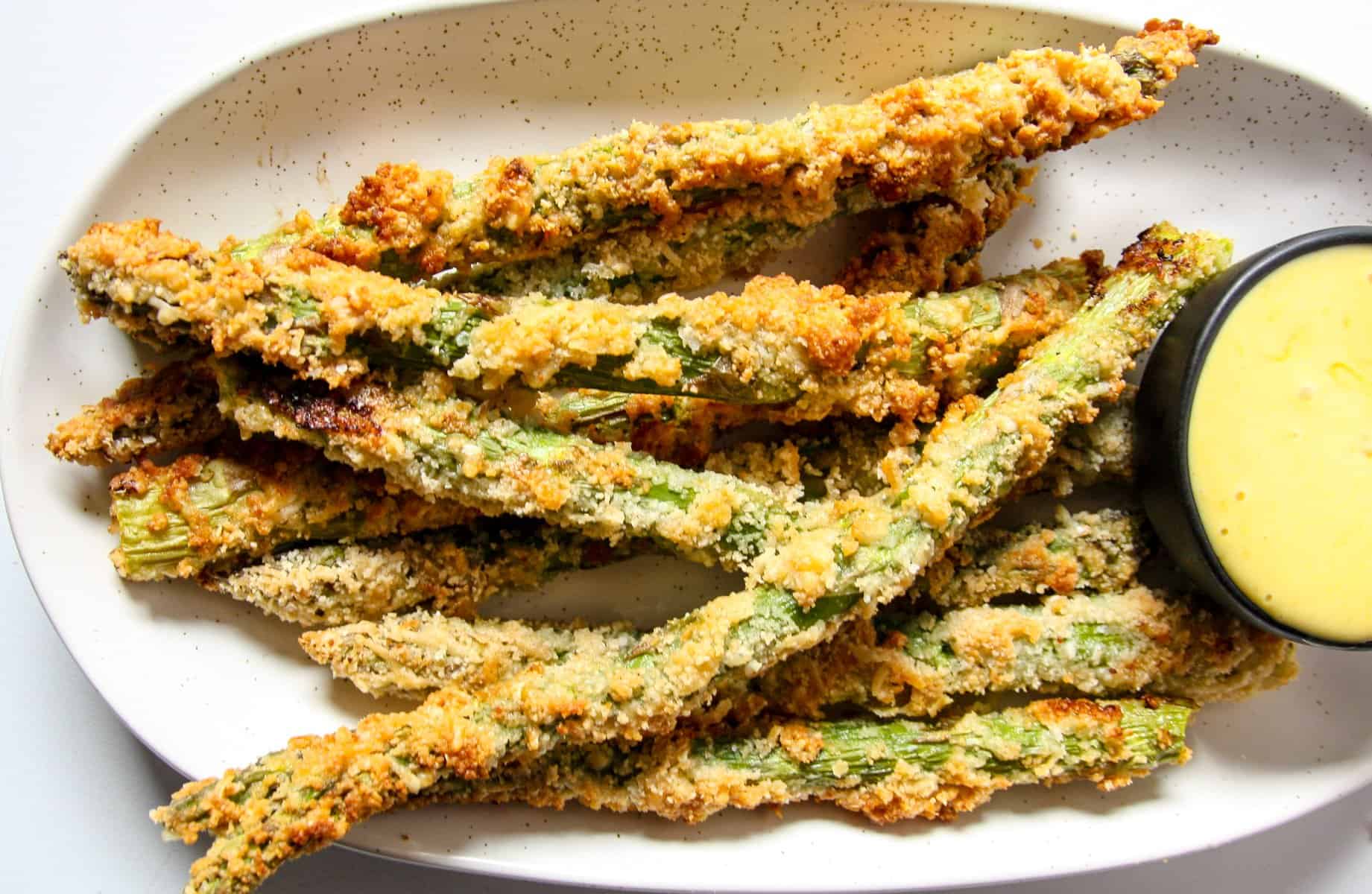 A plate of asparagus fries with a small dish of dipping sauce.