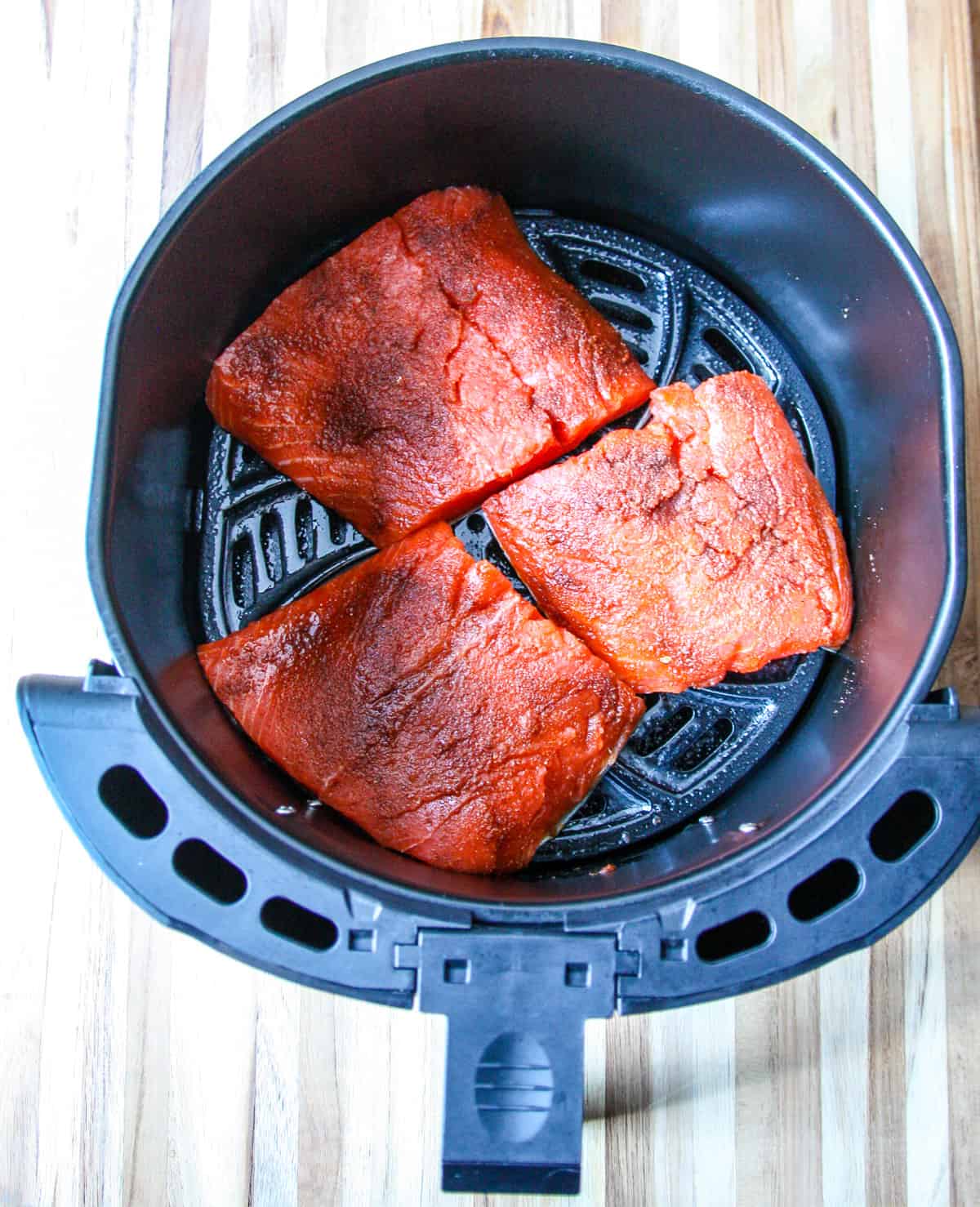 Three salmon fillets in an air fryer basket ready to be cooked.