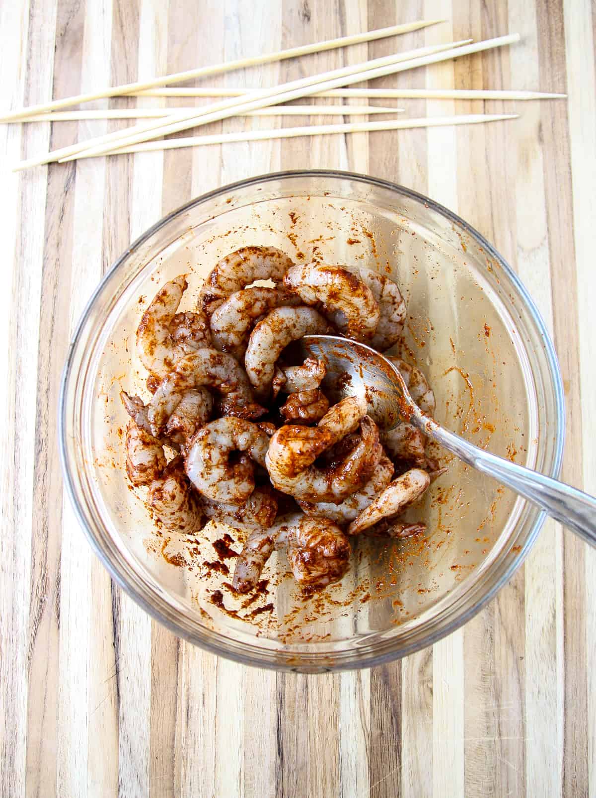 Shrimp being tossed in chilli lime marinade in a glass bowl.