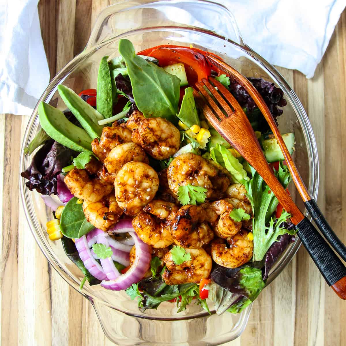 A salad in a glass bowl topped with grilled prawns.