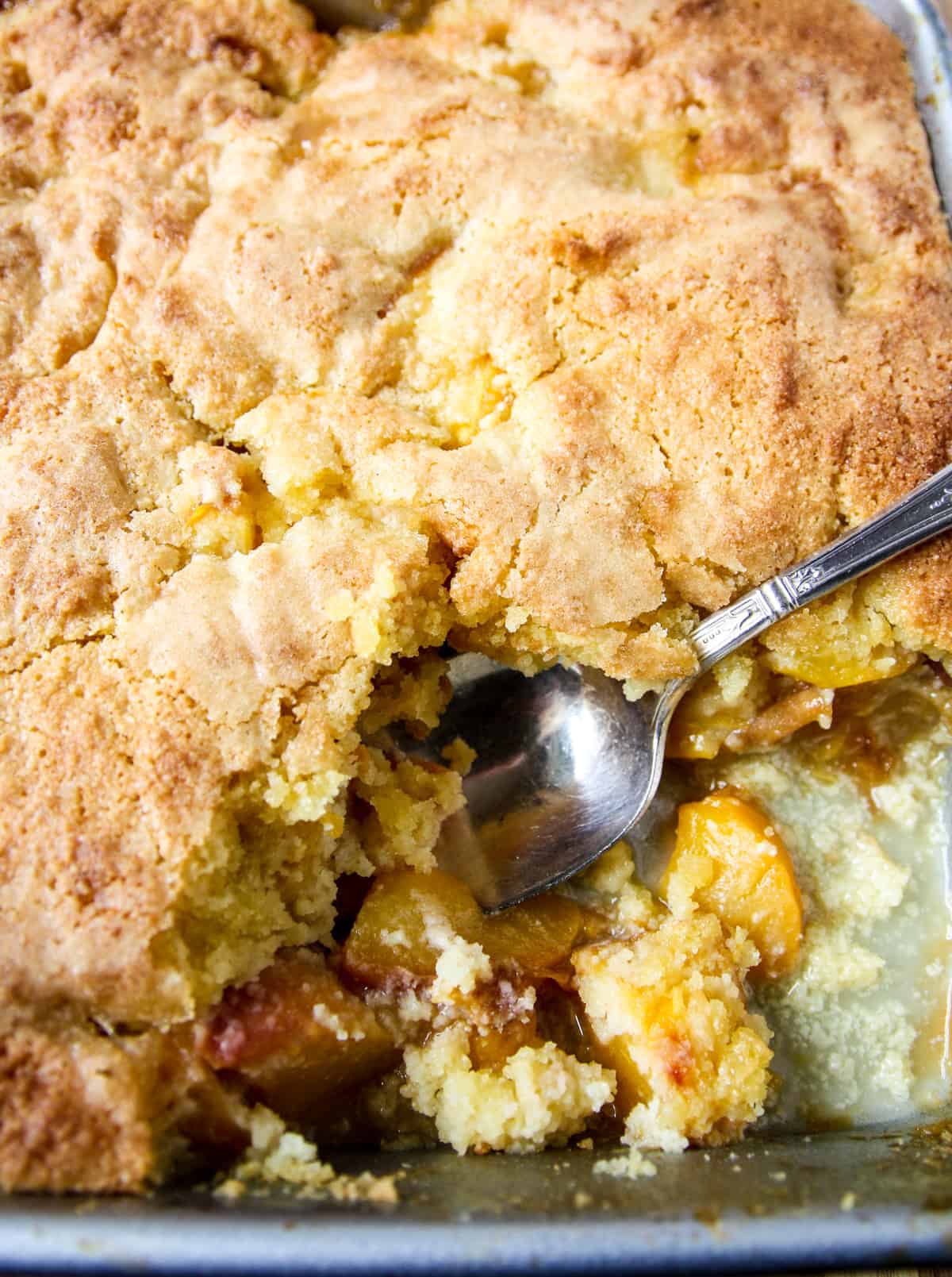 A close up of a pan of peach cobbler with one portion removed.