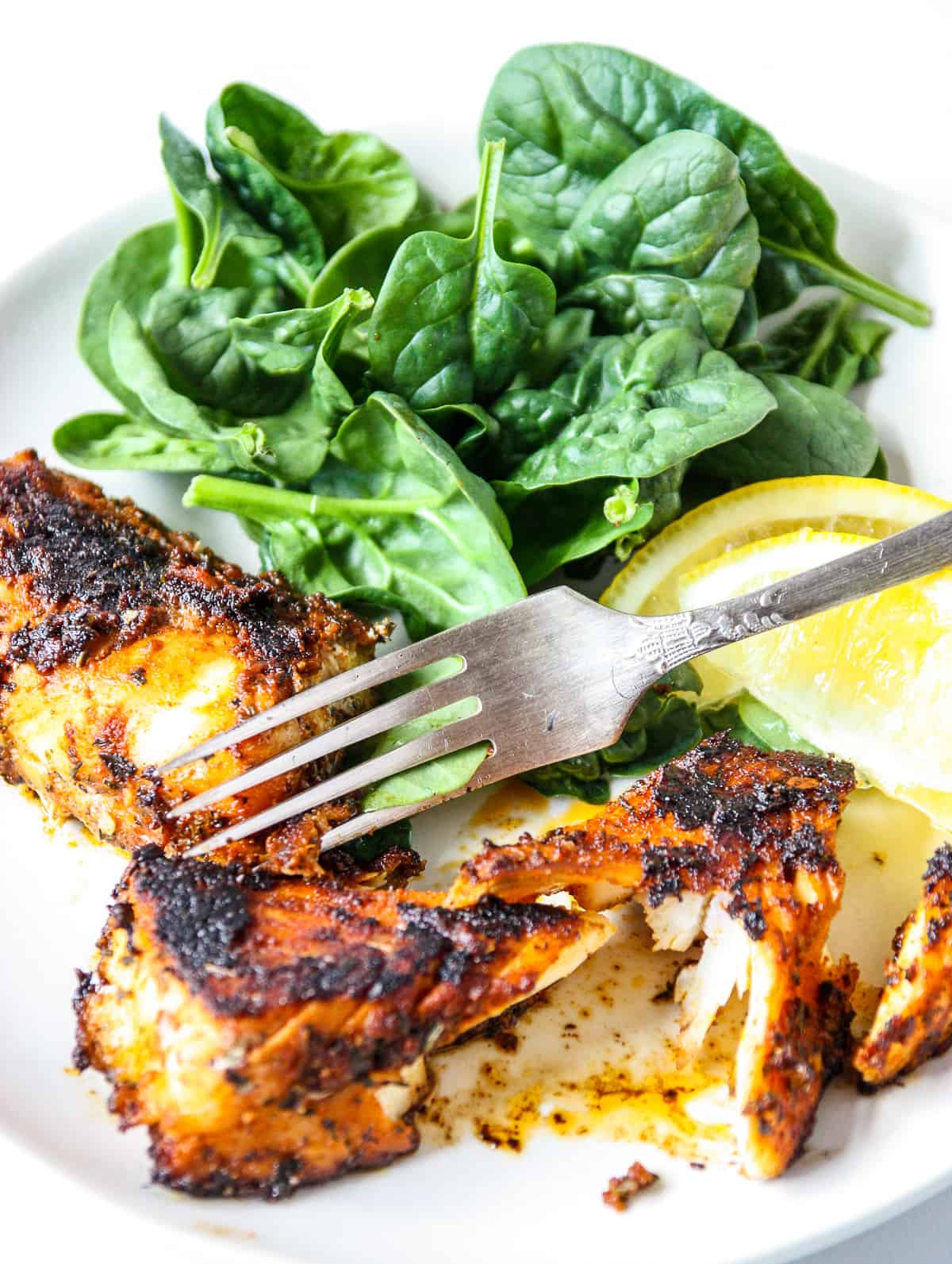 A silver fork cutting into a pan seared fish fillet.