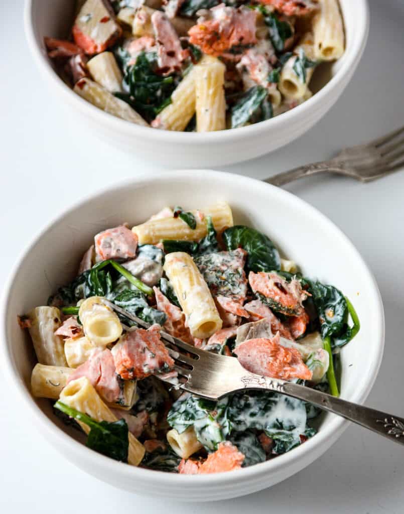 Salmon spinach pasta in a white bowl with a silver fork.
