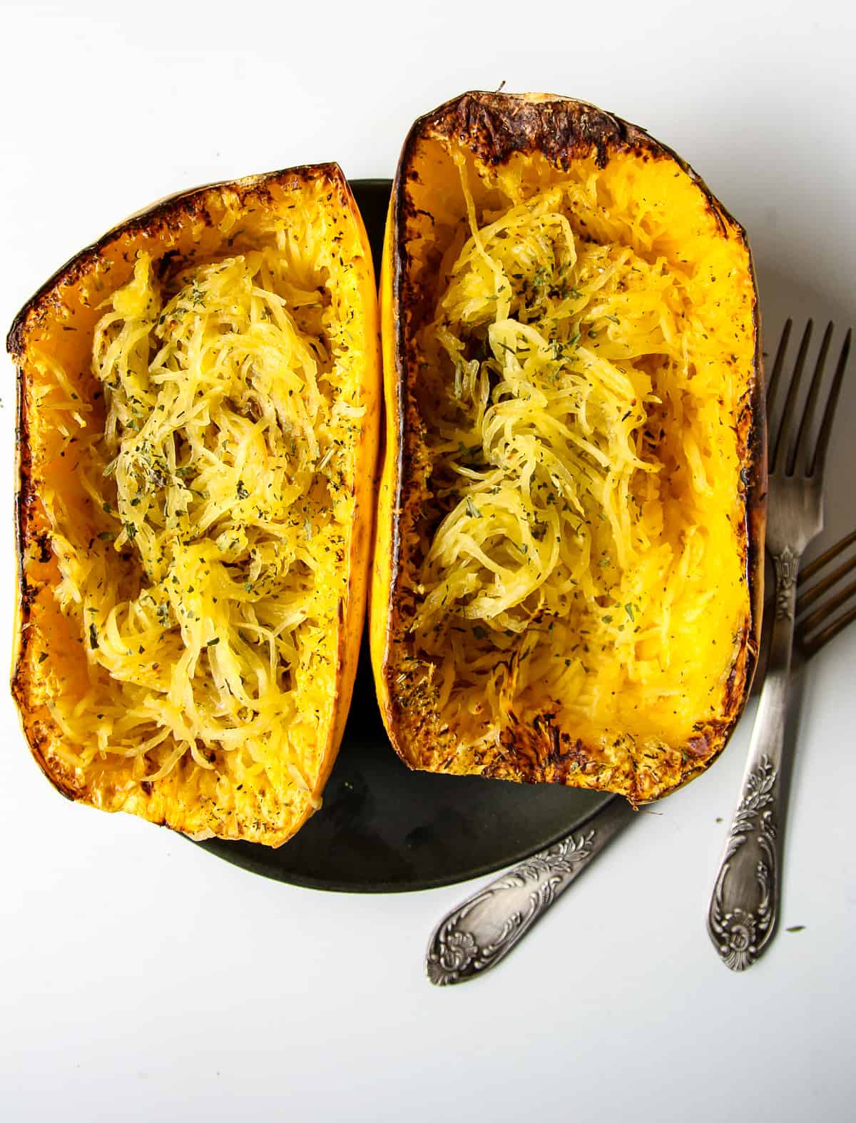 Two cooked spaghetti squash halves on a black plate.