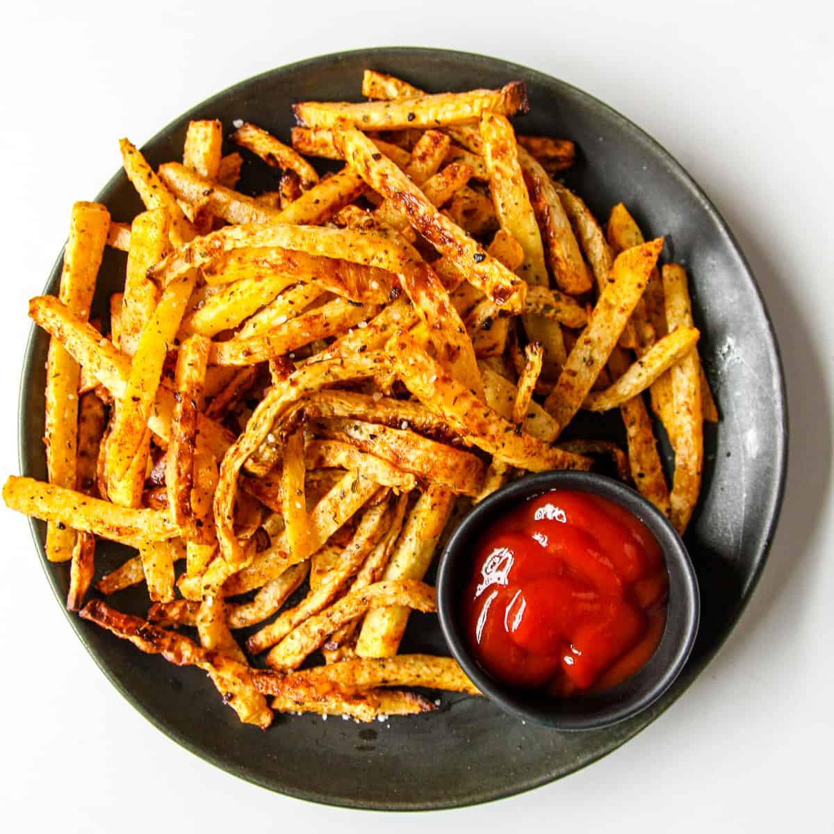 Rutabaga Fries piled on a black plate with a small dish of ketchup.