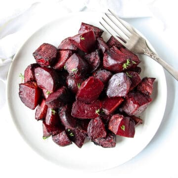 Cubed roasted red beets on a white plate with a silver fork.