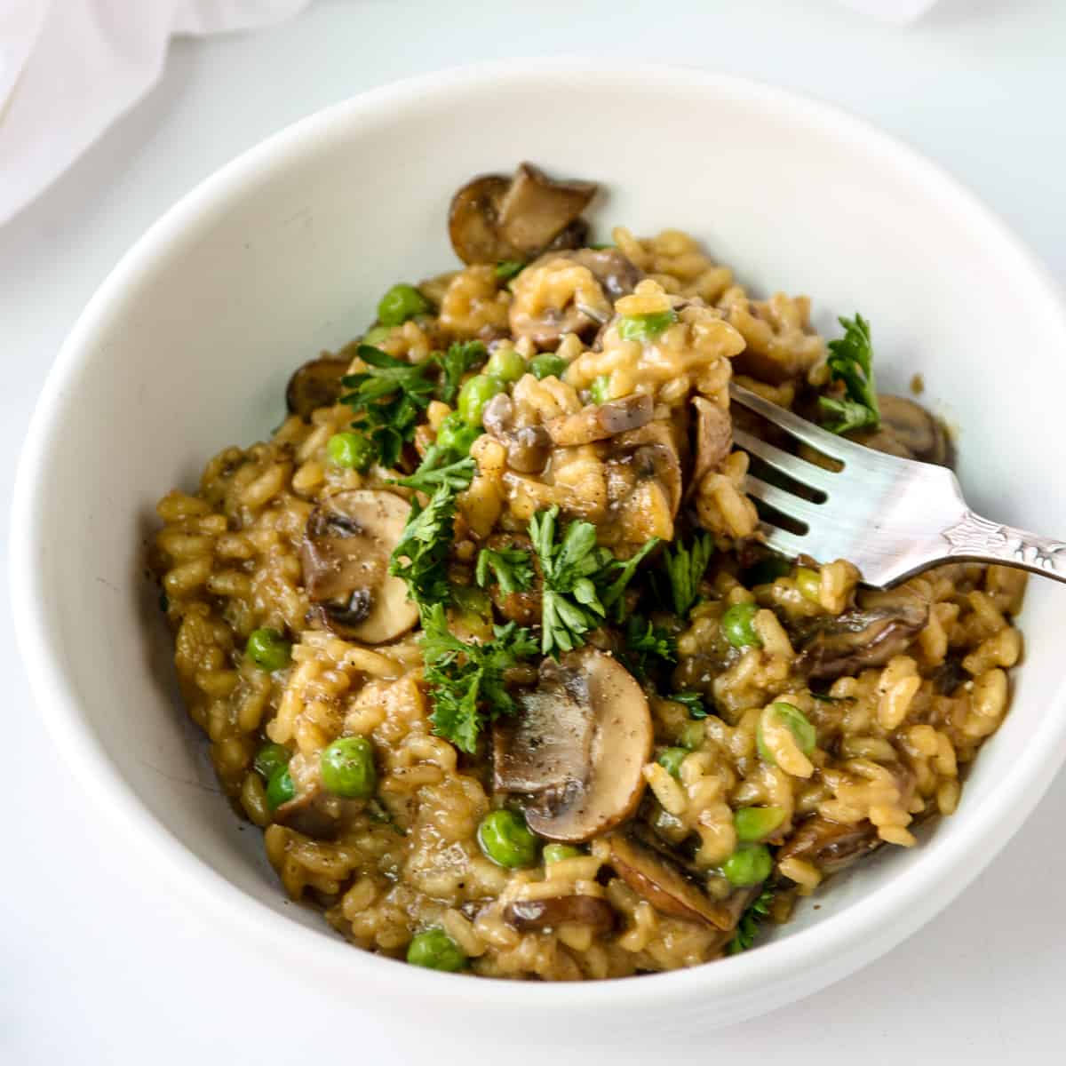 Mushroom pea risotto in a white bowl with a silver fork.