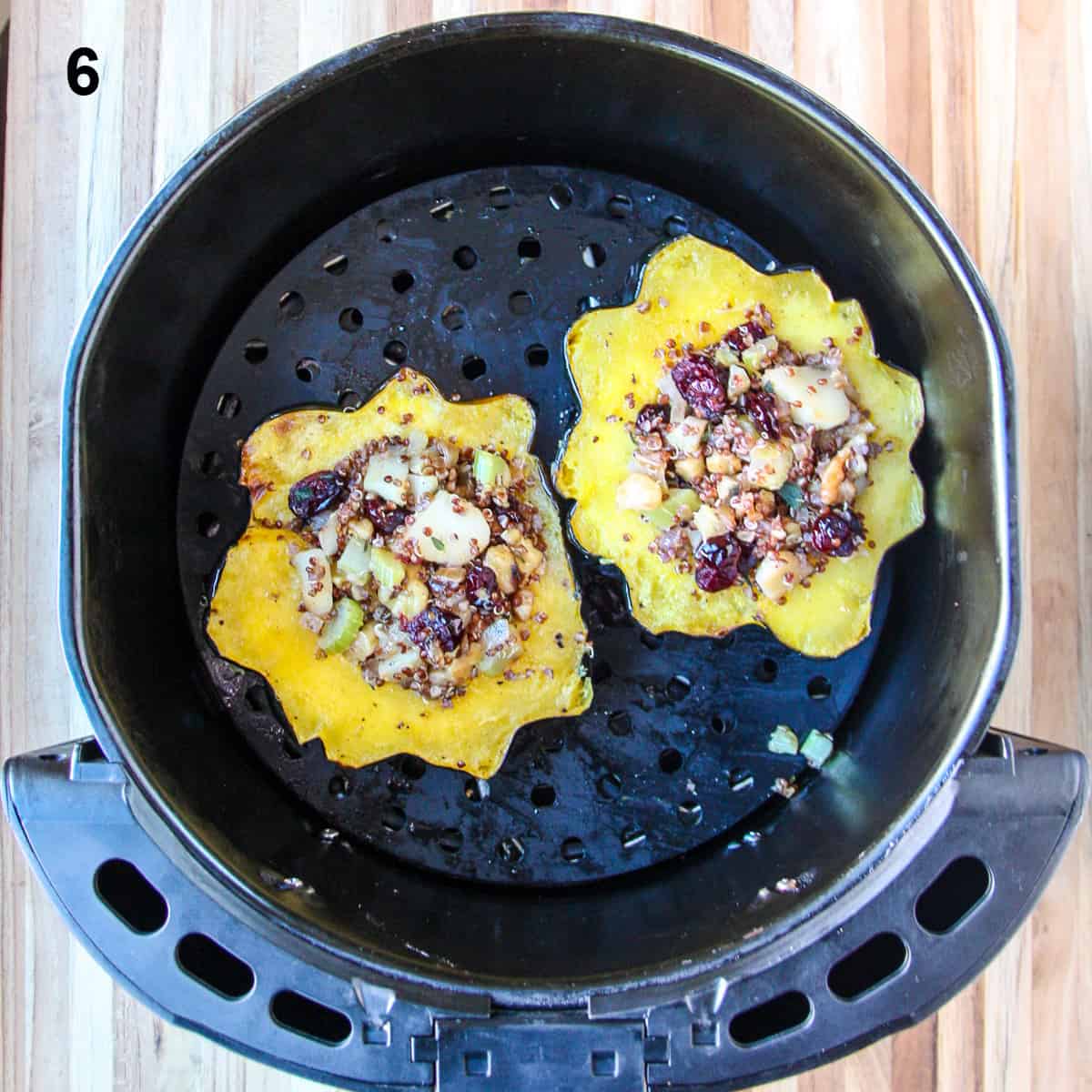 Two filled acorn squash halves in the air fryer basket after cooking.