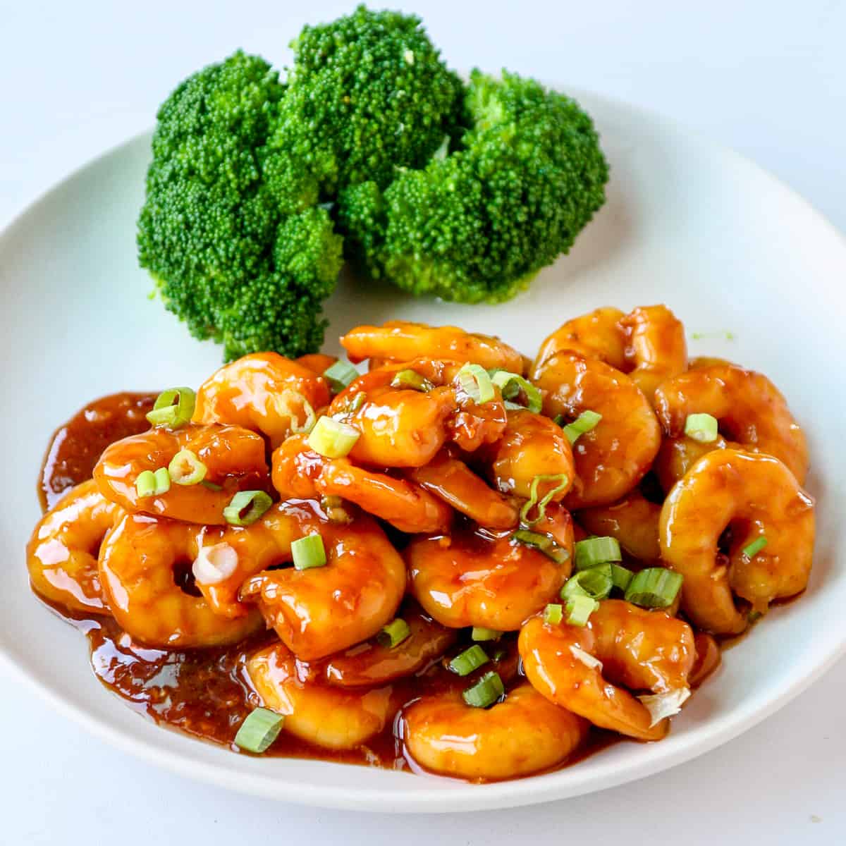 General Tso shrimp on a white plate with a side of steamed broccoli.