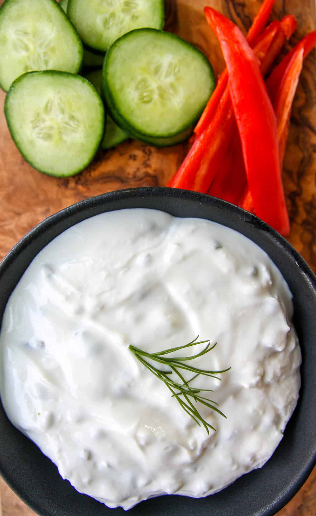 Creamy tzatziki sauce in a black dish, surrounded by vegetable slices.