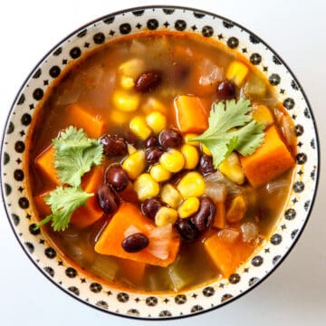 Sweet potato soup with black beans and corn in a black and white bowl.