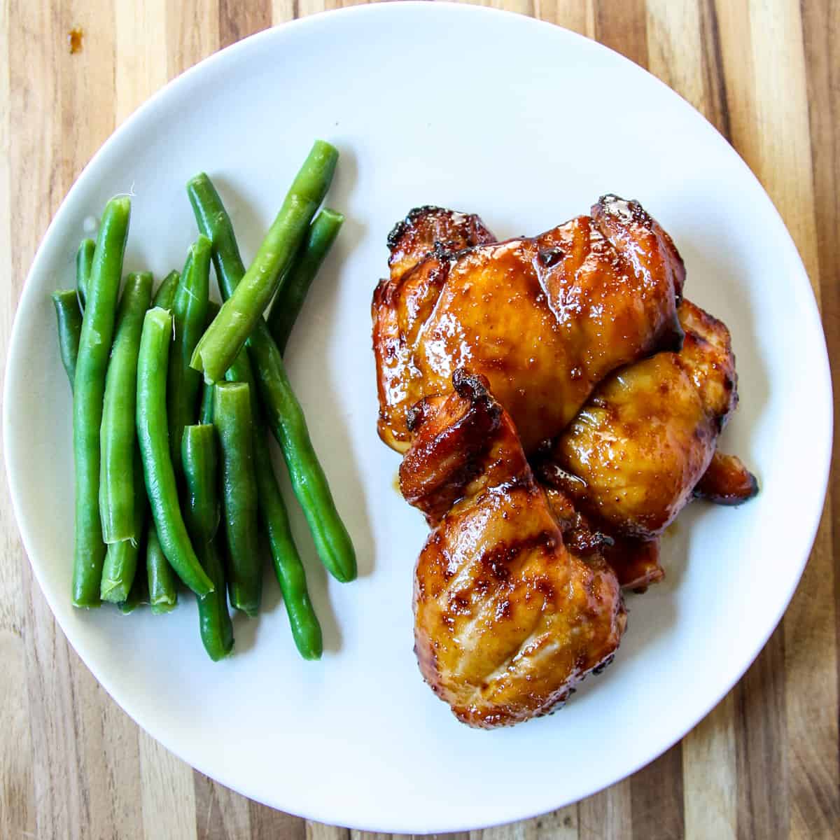Three pieces of glazed chicken on a white plate.