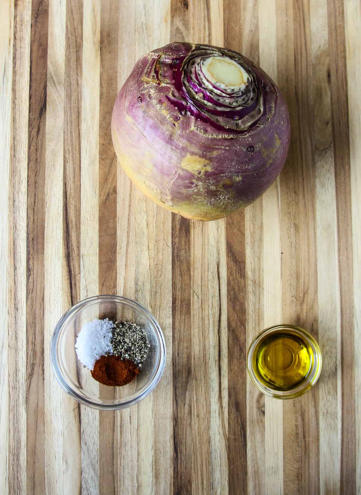 A whole raw rutabaga on a cutting board with a small bowl of seasonings and a small dish of oil.