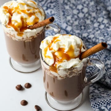 Two glass mugs with Rumchata hot chocolate, topped with whipped cream.