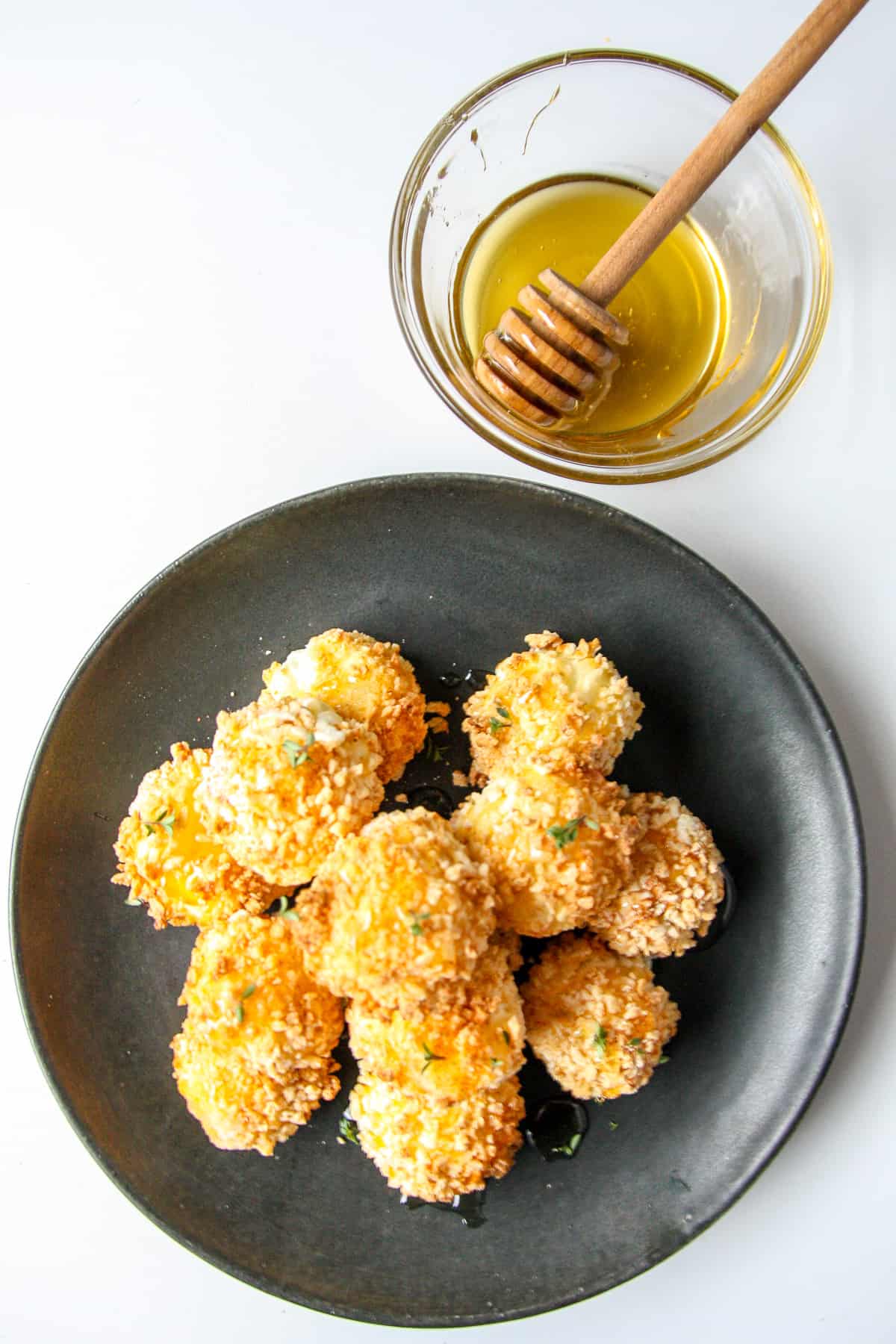 A plate of finished goat cheese balls beside a small dish of honey.